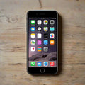 An Apple iPhone 7 Black 32GB Unlocked Smartphone with a black frame rests on a wooden surface, showing its vivid home screen—a certified quality Apple device offering great value.