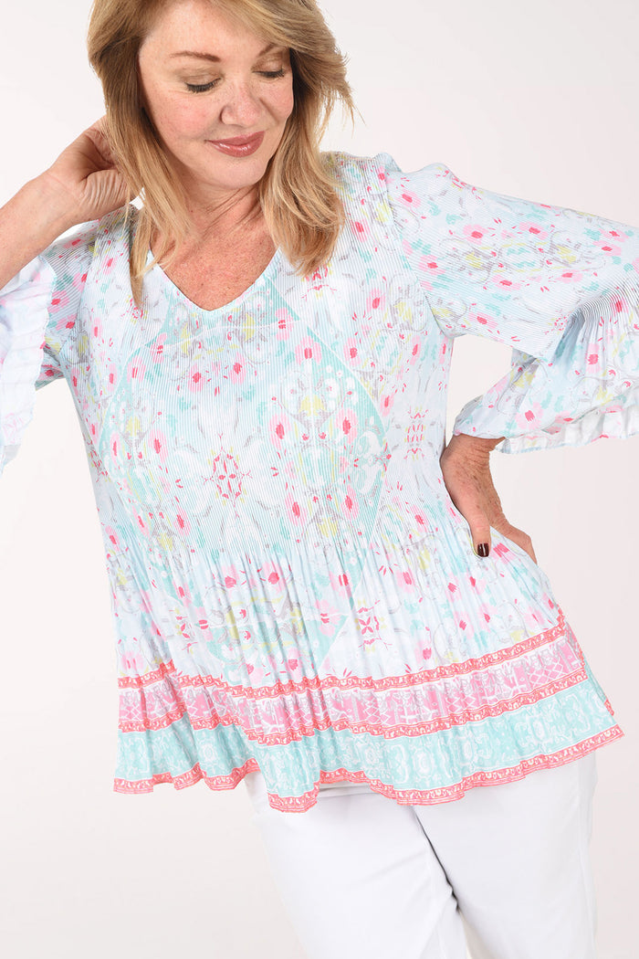 Woman wearing a light blue floral print top with pink trim on a white background